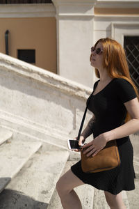Red hair girl walking up the stairs holding a phone in sunny day