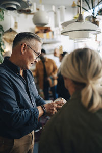 Senior store owner telling price to customer doing shopping at antique shop