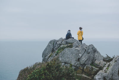 Rear view of friends on cliff by sea against cloudy sky