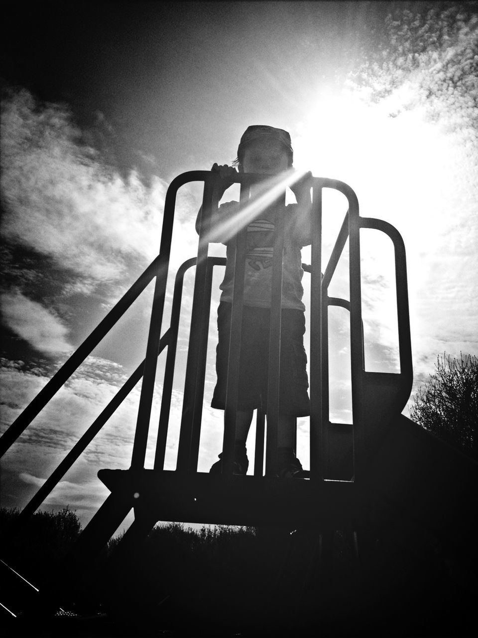 low angle view, sky, sunlight, sun, railing, silhouette, sunbeam, built structure, cloud - sky, outdoors, leisure activity, lens flare, cloud, day, standing, architecture, sunset, tree