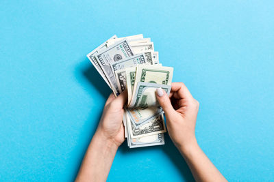 Close-up of hands holding paper currency against blue background