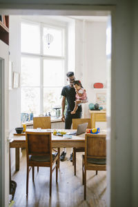 Young man carrying daughter seen through doorway at home