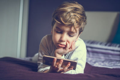 Boy looking at mobile phone on bed