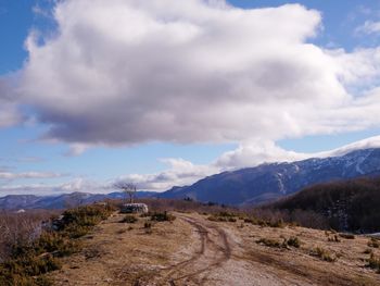 Dirt road leading towards mountains against sky
