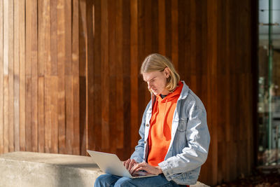 Portrait of young man using laptop while standing against wall