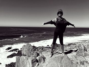 Full length of young woman with arms outstretched standing on rock at beach