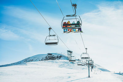 People sitting on overhead cable car over snowcapped mountains against sky