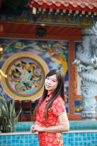 Portrait of smiling young woman standing against wall