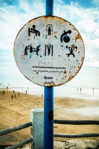 Close-up of information sign on beach against sky