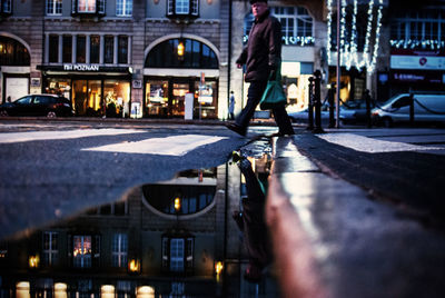 Reflection of man walking in city on puddle during sunset