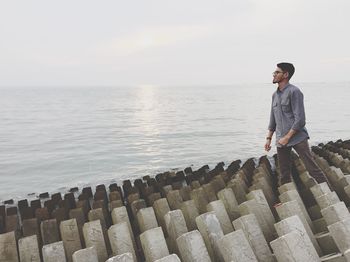 Man standing on concrete groynes by sea against sky