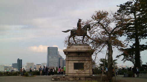 Statue in city against cloudy sky