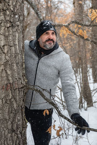 Portrait of man standing by tree trunk during winter