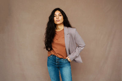Ethnic female in casual jacket looking at camera standing on brown background in studio