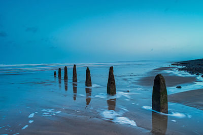 Wooden posts in sea against blue sky