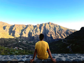 Rear view of man looking at mountains against clear sky