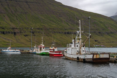 Sailboats moored on sea by mountains against sky