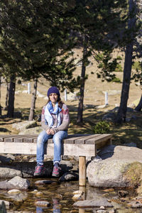 Full length of woman sitting on boardwalk against trees in forest