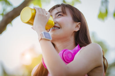 Low angle view of smiling young woman drinking water while standing outdoors