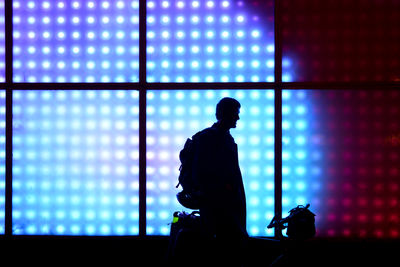 Silhouette man standing against illuminated window