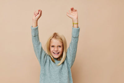 Young woman with arms raised against pink background