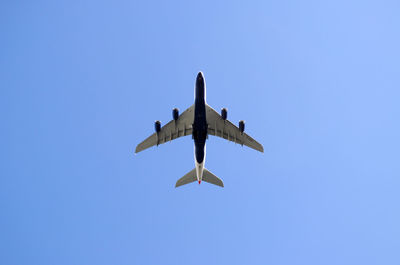 Low angle view of airplane flying against clear blue sky