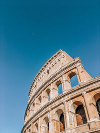 Low angle view of building, colosseum silhouette against clear blue sky 