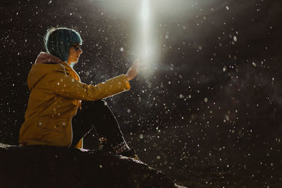 Side view of man standing on wet umbrella at night