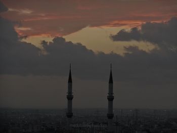 Communications tower in city against sky at sunset