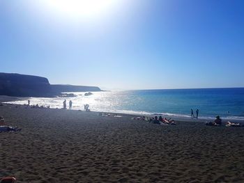 People on beach against clear blue sky