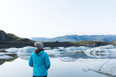 Rear view of woman standing by lake against clear sky