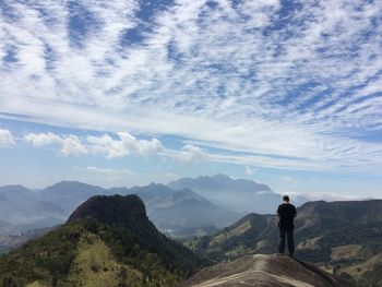 Rear view of man standing on mountain peak against sky