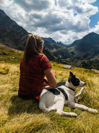 Woman with dog sitting on mountain against sky