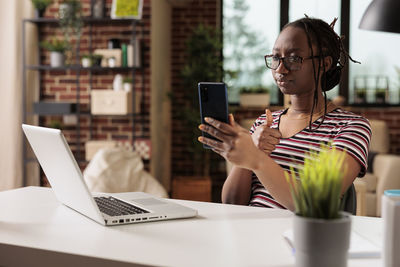 Young woman using phone while sitting on table