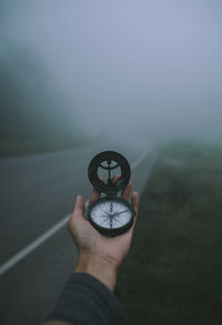 Close-up of hand holding navigational compass on road during foggy weather