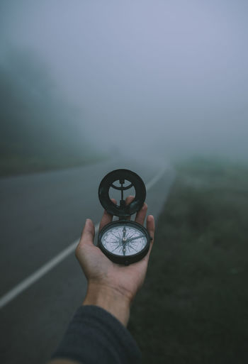 Close-up of hand holding navigational compass on road during foggy weather