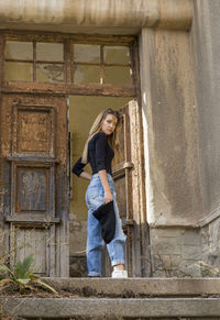 Low angle view of young woman standing by doorway at abandoned building