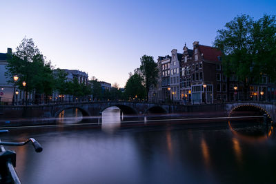 Bridge over river by buildings against sky in city