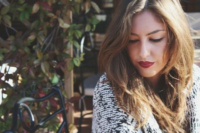 Close-up of young woman with brown hair against plants at park on sunny day