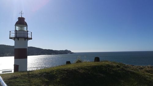 Lighthouse by sea against clear sky