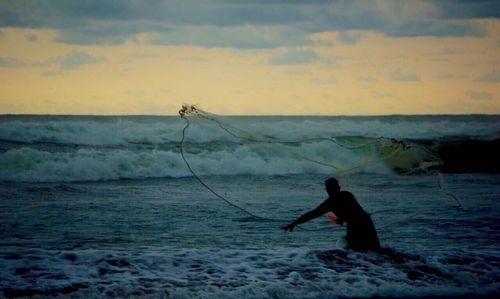 Silhouette man fishing in sea against sky during sunset