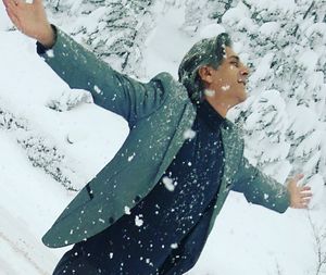 Man standing with arms outstretched during snowfall