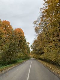Country road amidst trees against sky