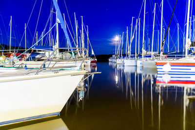 Sailboats moored at harbor against blue sky