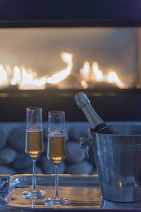 Champagne flutes by ice bucket against burning fireplace