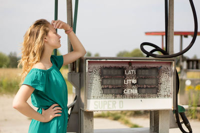 Young woman standing by gas station against sky