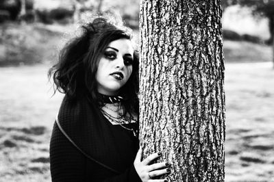 Portrait of gothic woman standing by tree trunk