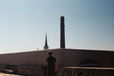 Rear view of man standing tower against sky