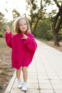 Cute funny child girl 4-5 year old wear bright pink sweater having fun playing in park outdoor.