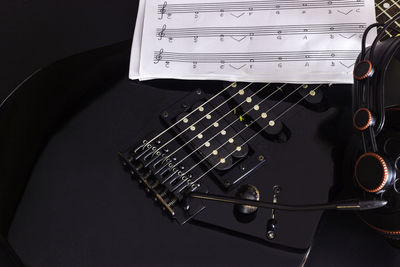 Close-up of guitar and sheet music against black background